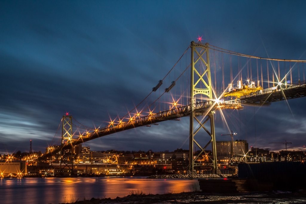 The Macdonald Bridge at night during the Big Lift. A gantry for replacing deck segments is seen lowering a segment to a barge beneath the bridge.