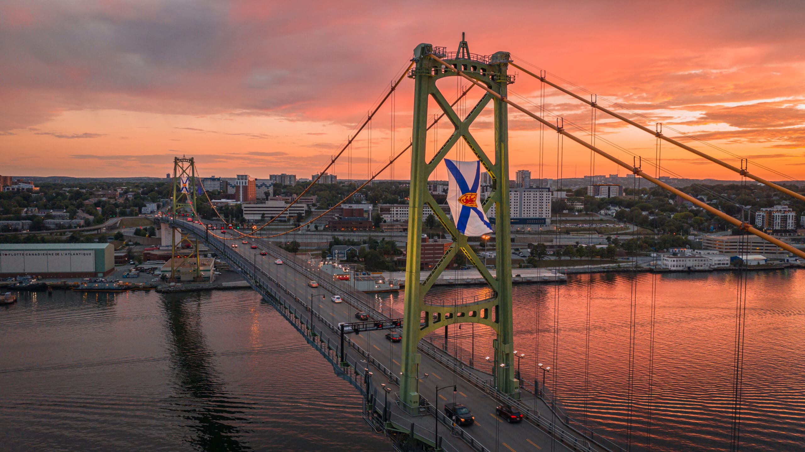 A photo of the Macdonald Bridge in Halfiax at sunset with Nova Scotia flags flying from the towers.