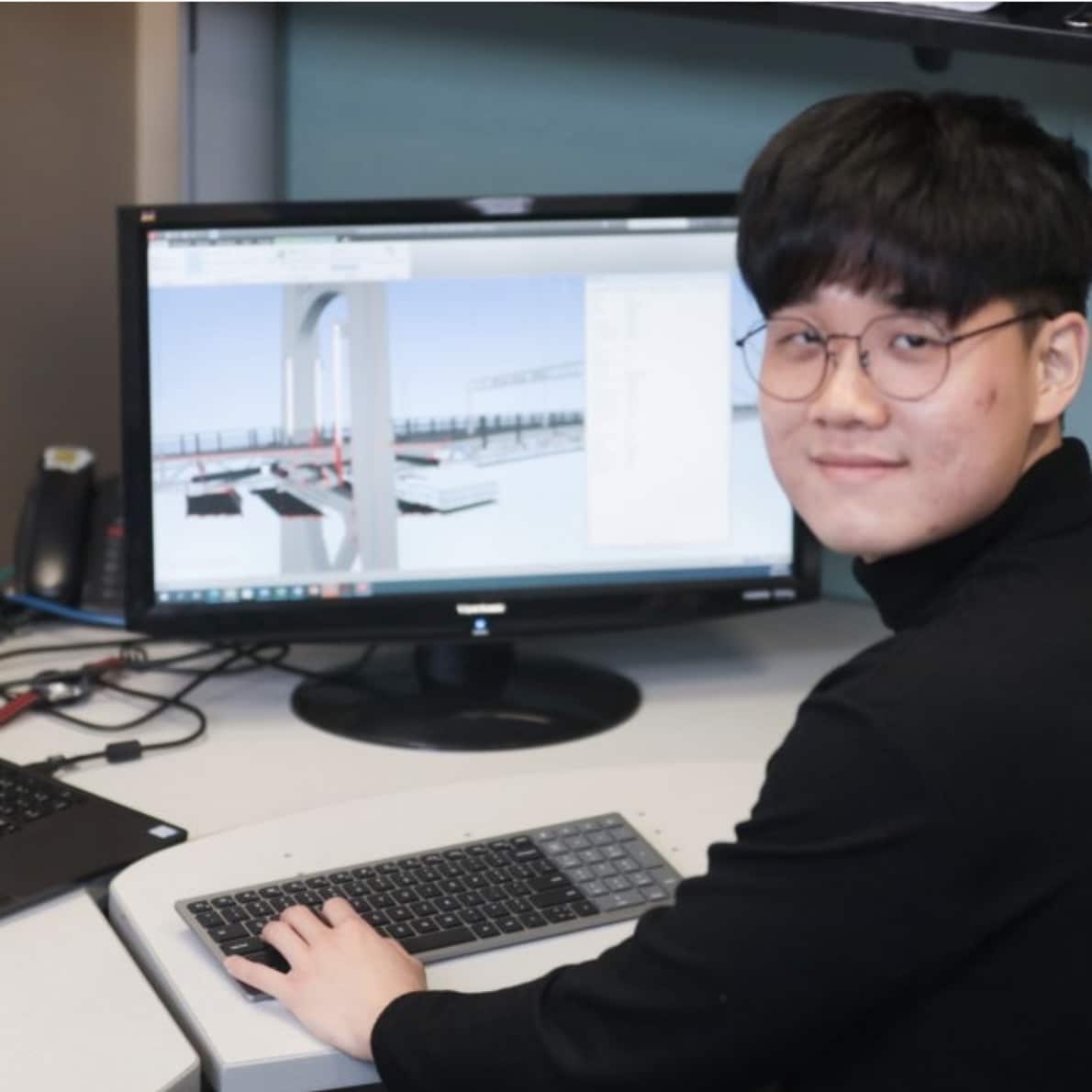Halifax Harbour Bridges engineering student Dong Woo Seo sits in front of a screen showing a digital rendering of the Macdonald Bridge.