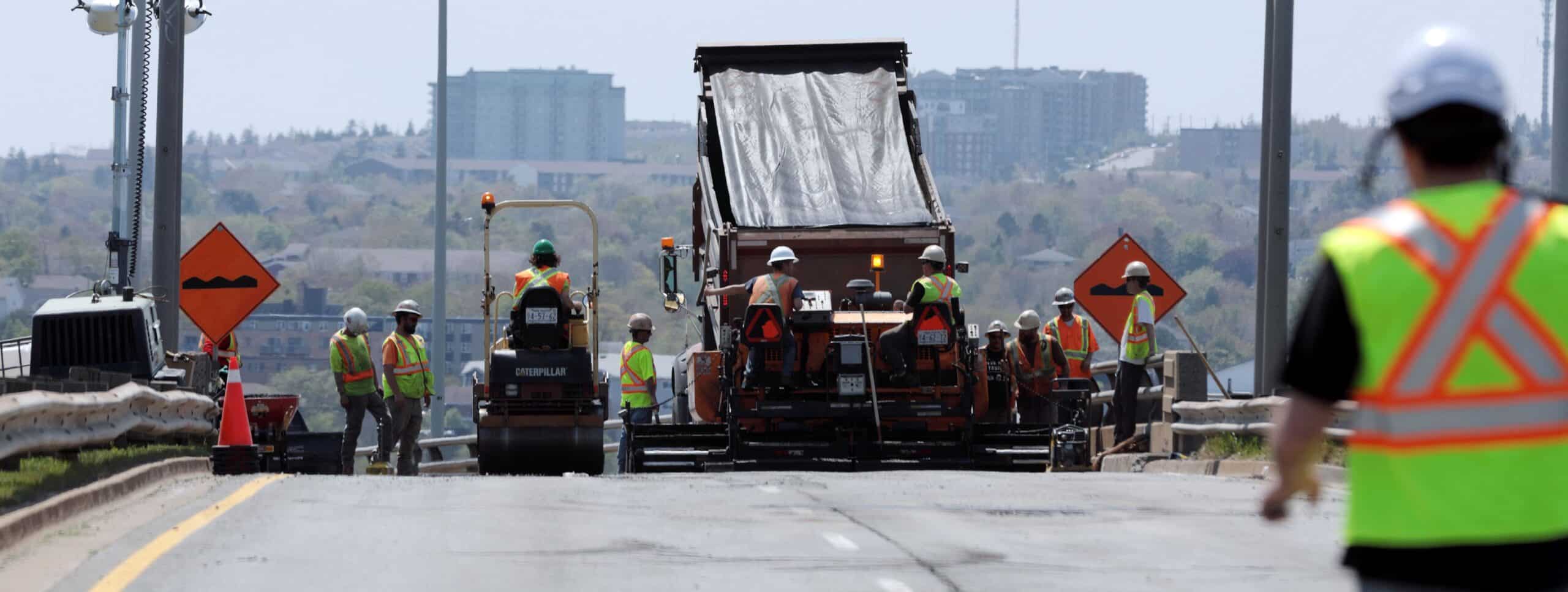 Paving crews roll asphalt on a section of roadway near the MacKay Bridge.